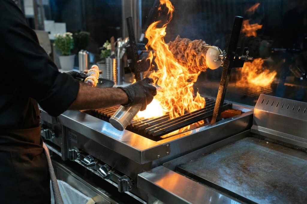 Chef grilling meat with spectacular flames in a modern kitchen setup.